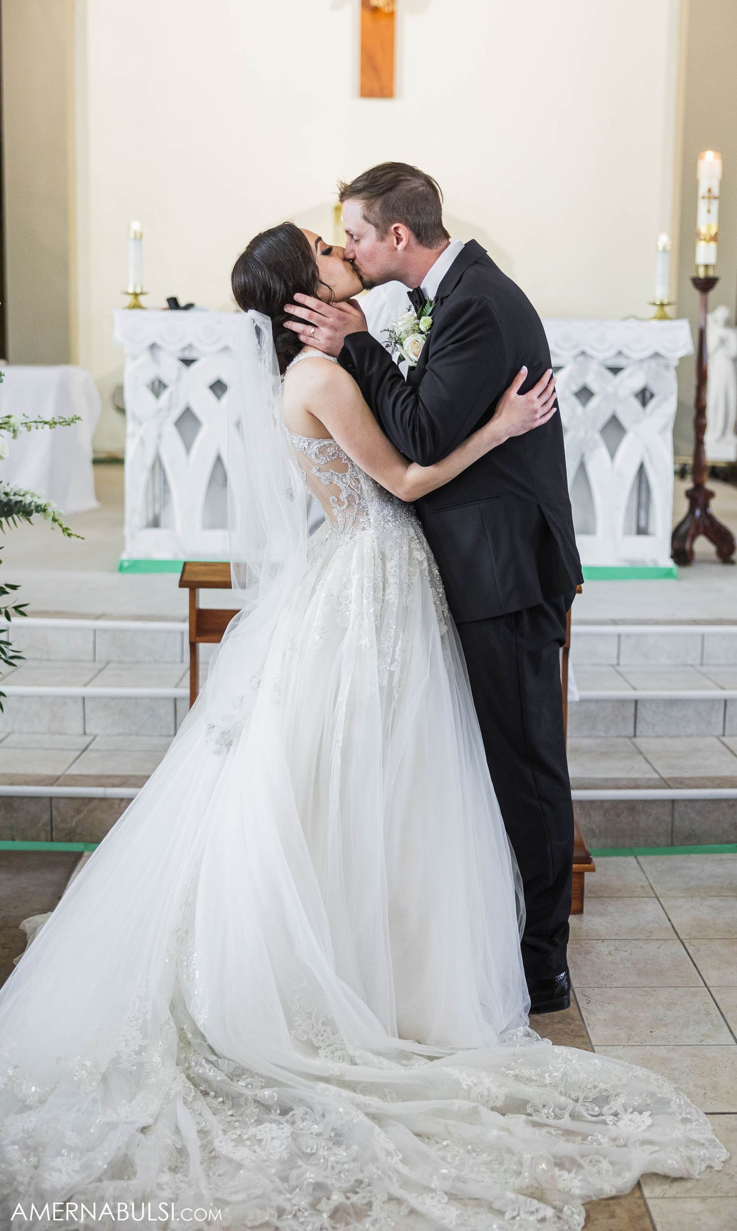 Newlyweds embrace in an intimate moment at a church altar with decorative white lattice panels.