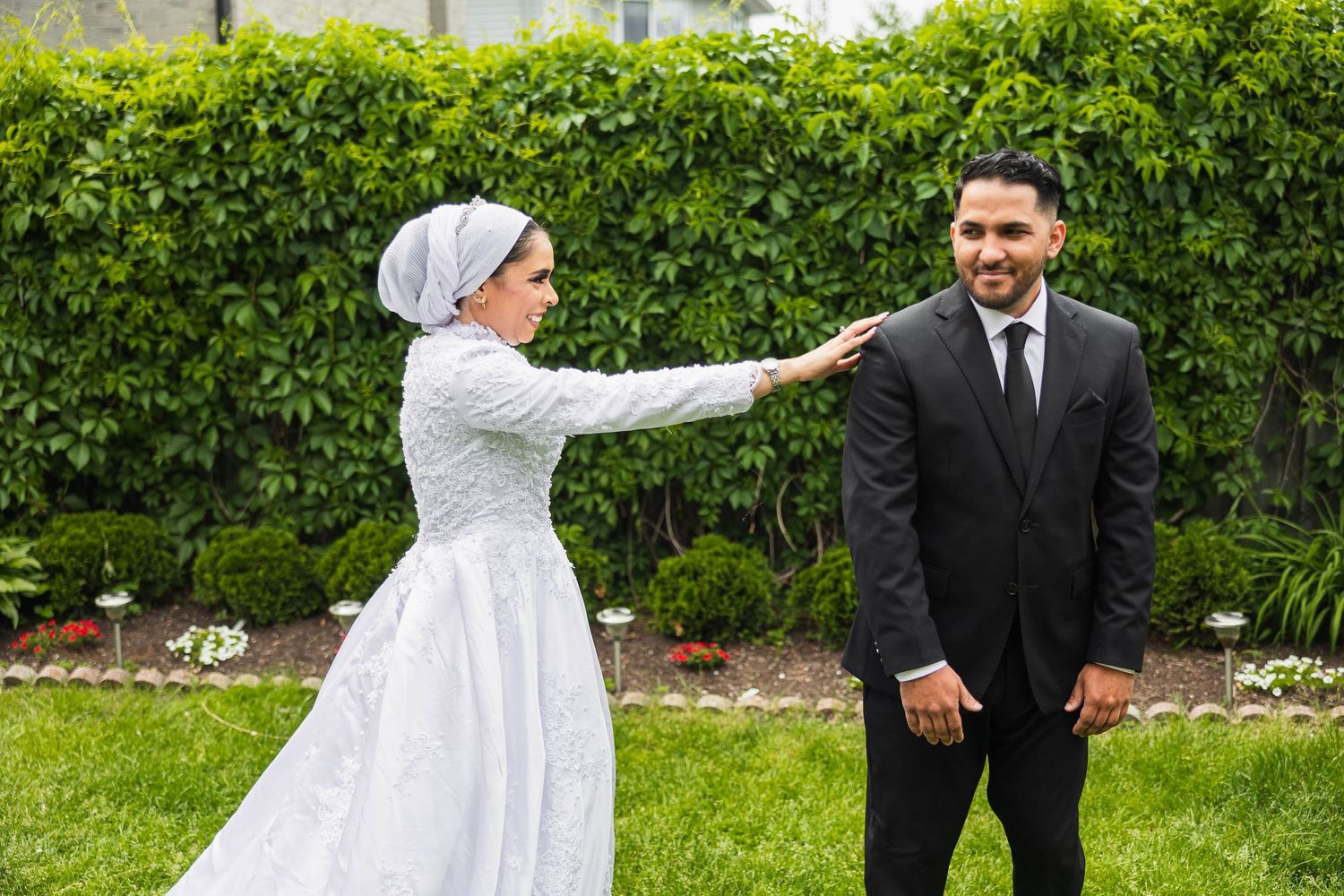 Bride in white dress touches groom's shoulder during outdoor wedding photo session.