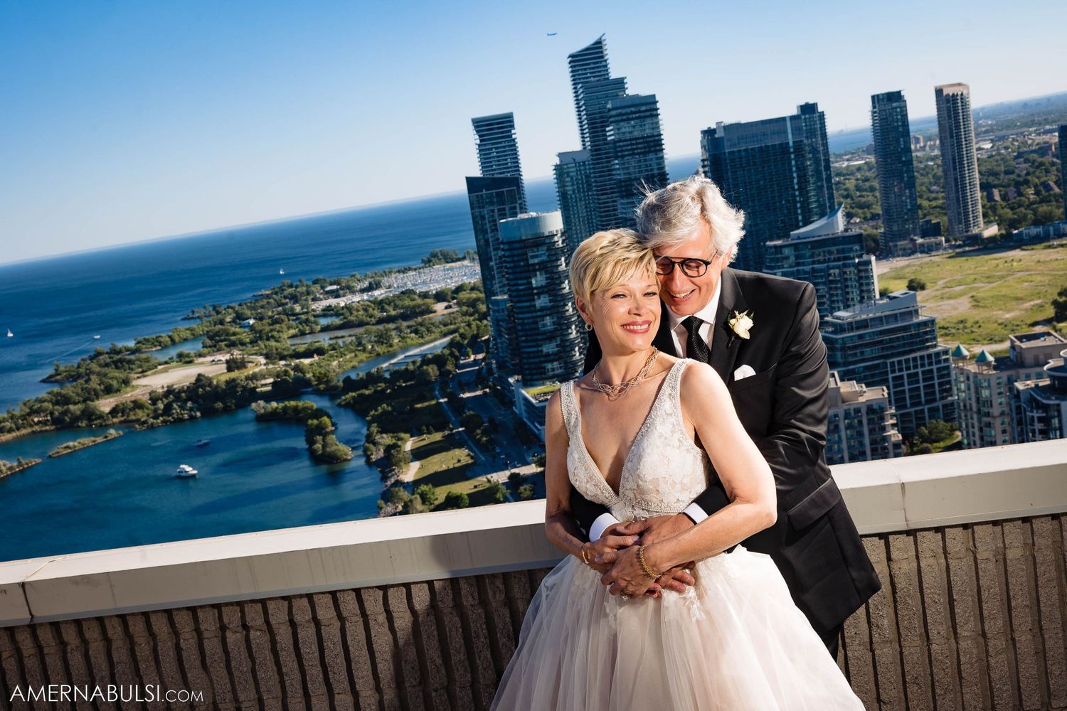 Wedding couple overlooking Toronto waterfront skyline from high-rise balcony.