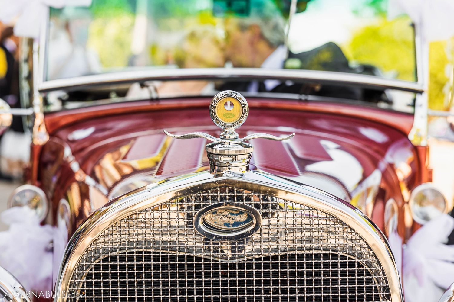 Close up detail of an ornate chrome radiator cap and grille on a vintage automobile.