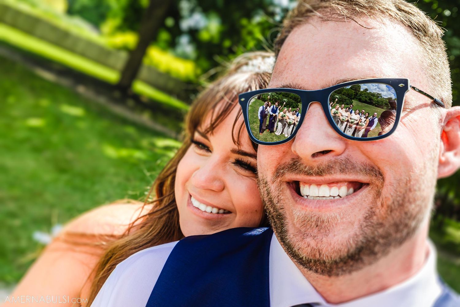 Close up photo showing a couple outdoors with one person wearing sunglasses reflecting trees in a park setting.