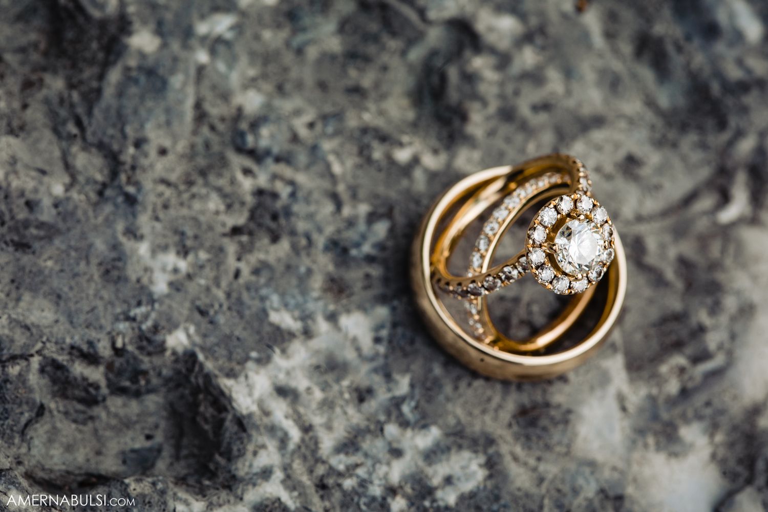 Gold wedding rings photographed on textured gray stone surface.