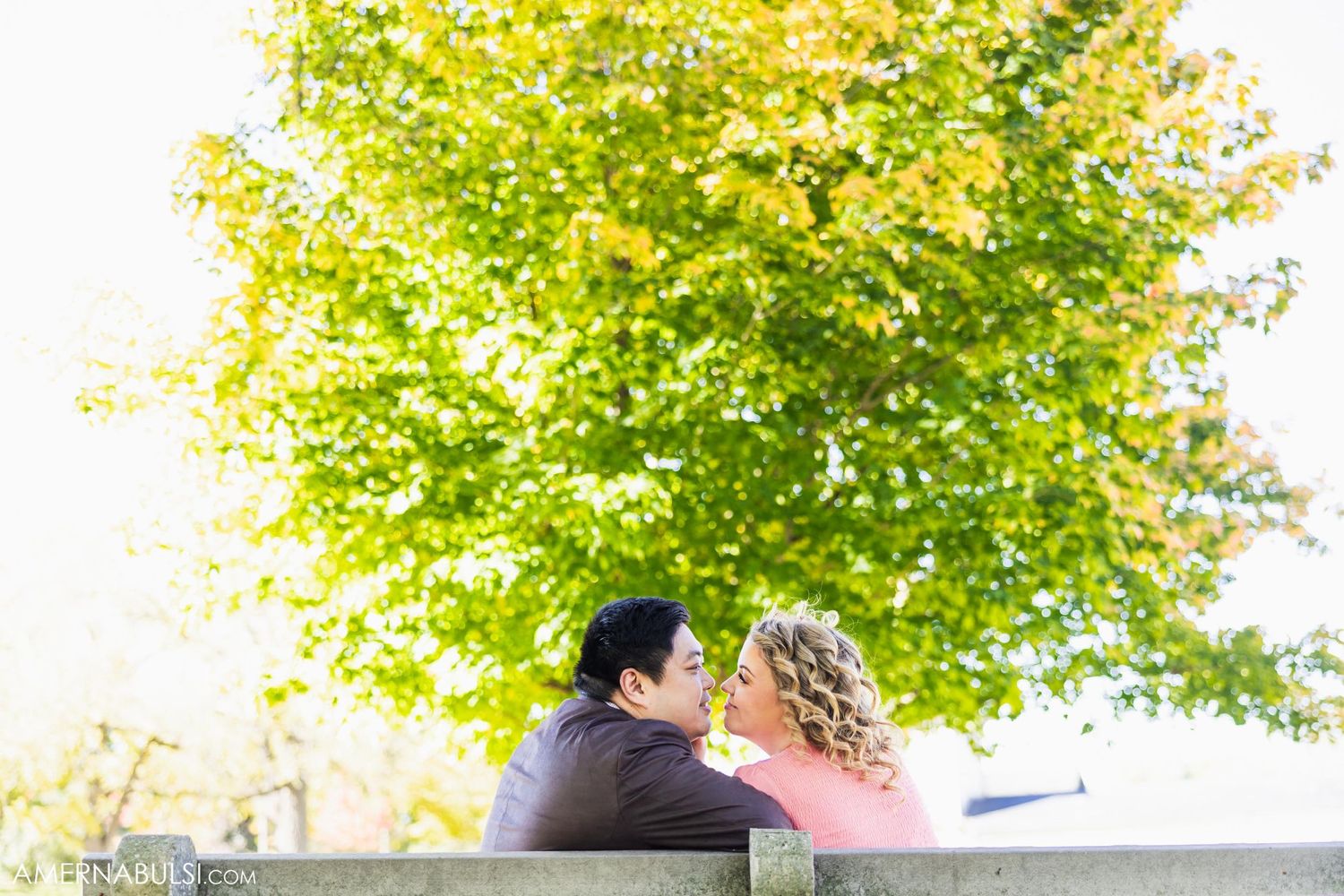 Romantic couple sitting close together on bench under vibrant yellow autumn tree.