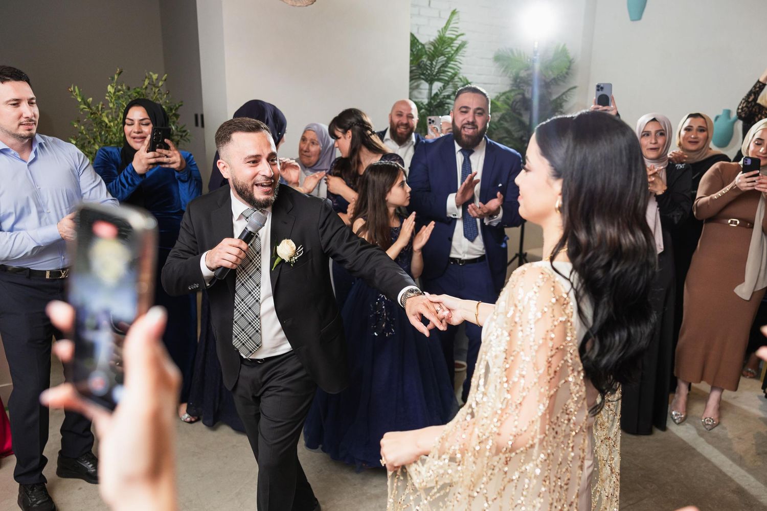 Guests dance and celebrate while others capture the moment on phones at an indoor event.