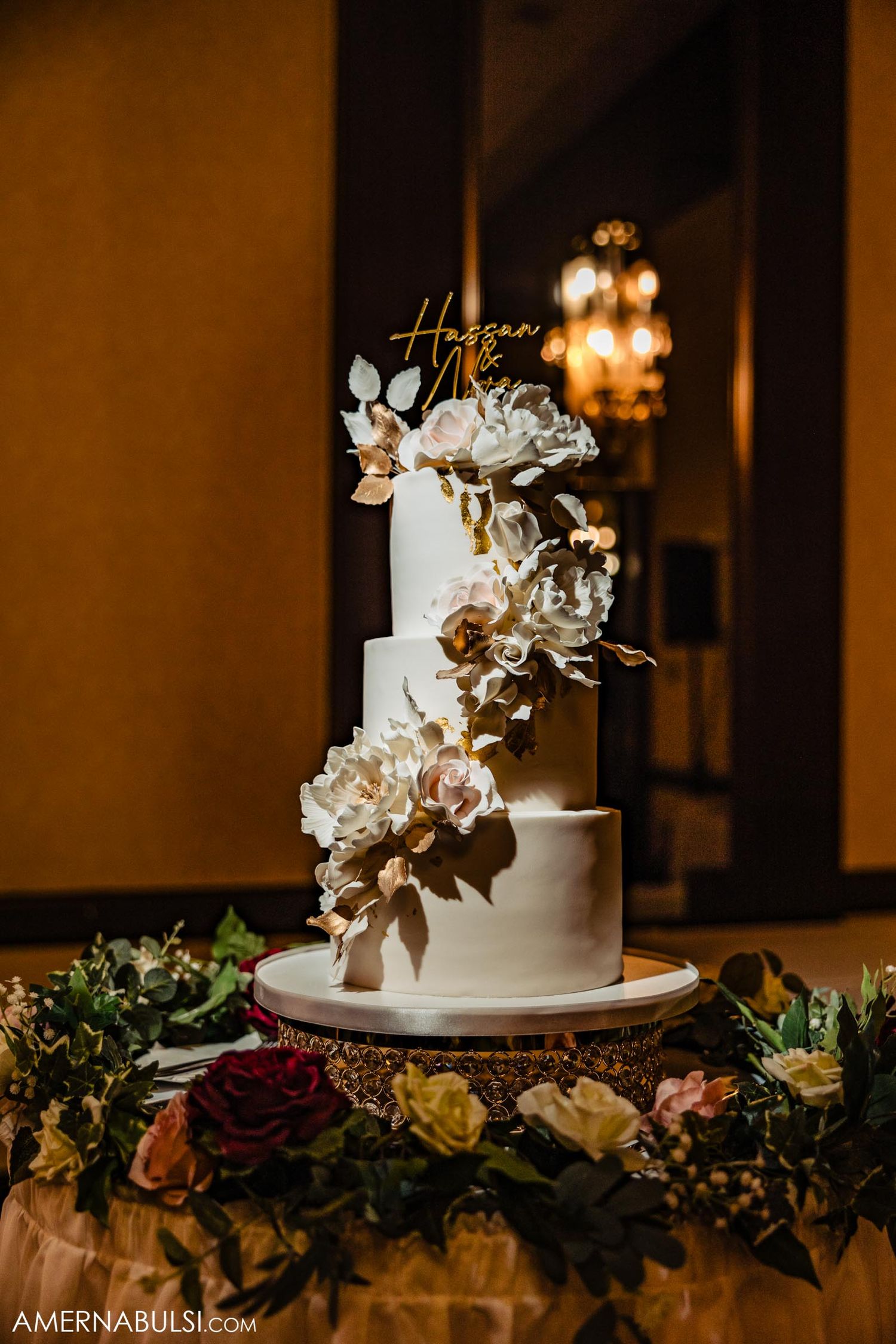 Elegant white wedding cake adorned with gold and ivory floral decorations on display.