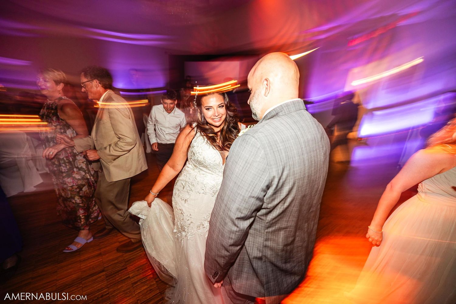 Wedding couple dancing together under colorful purple and orange lighting at their reception.
