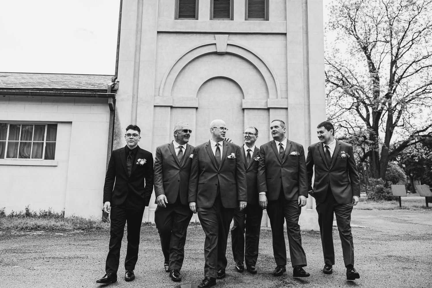 Wedding party in formal attire poses together outside historic church building.