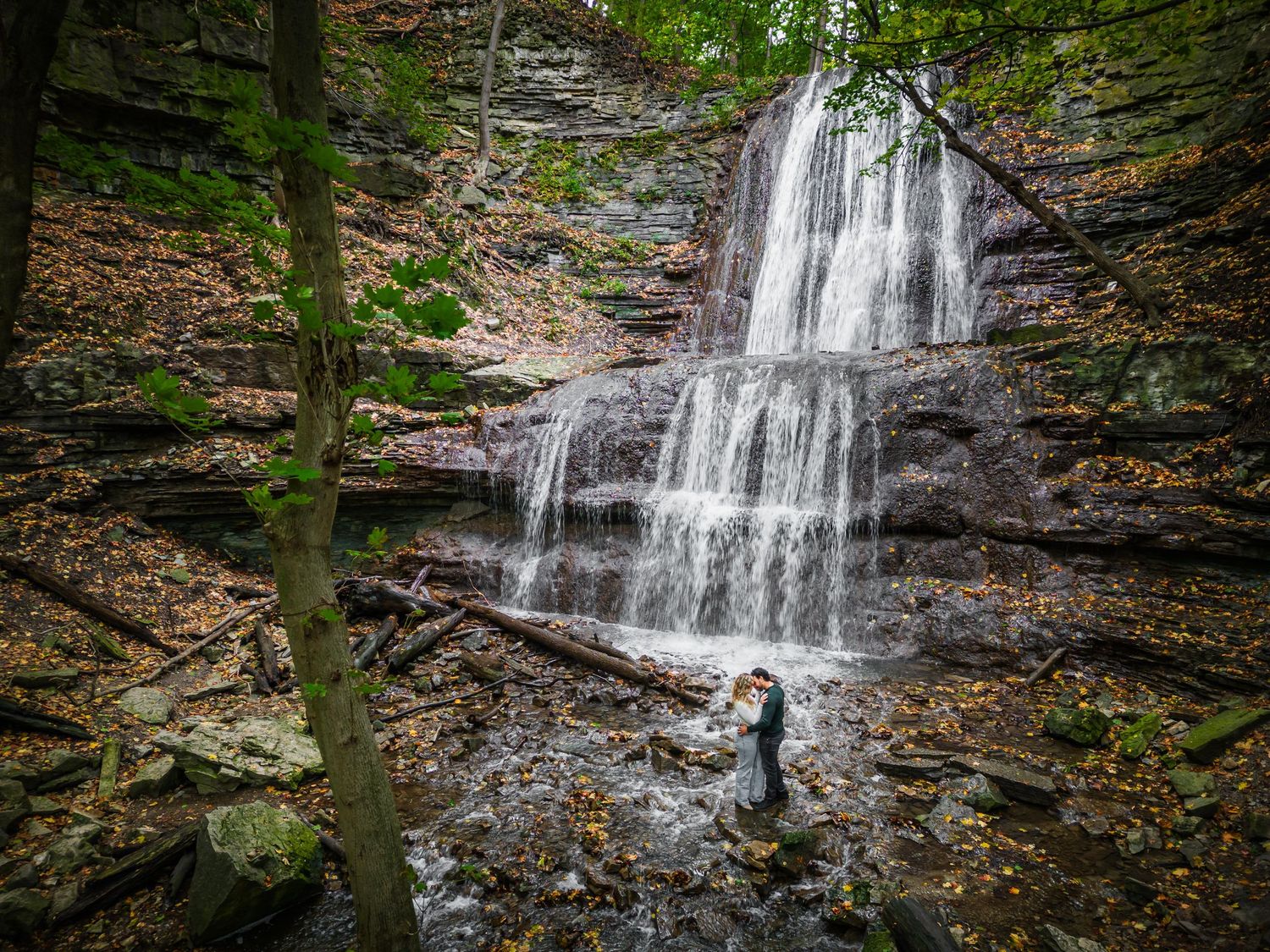 Couple standing beneath a majestic cascading waterfall in forest setting.