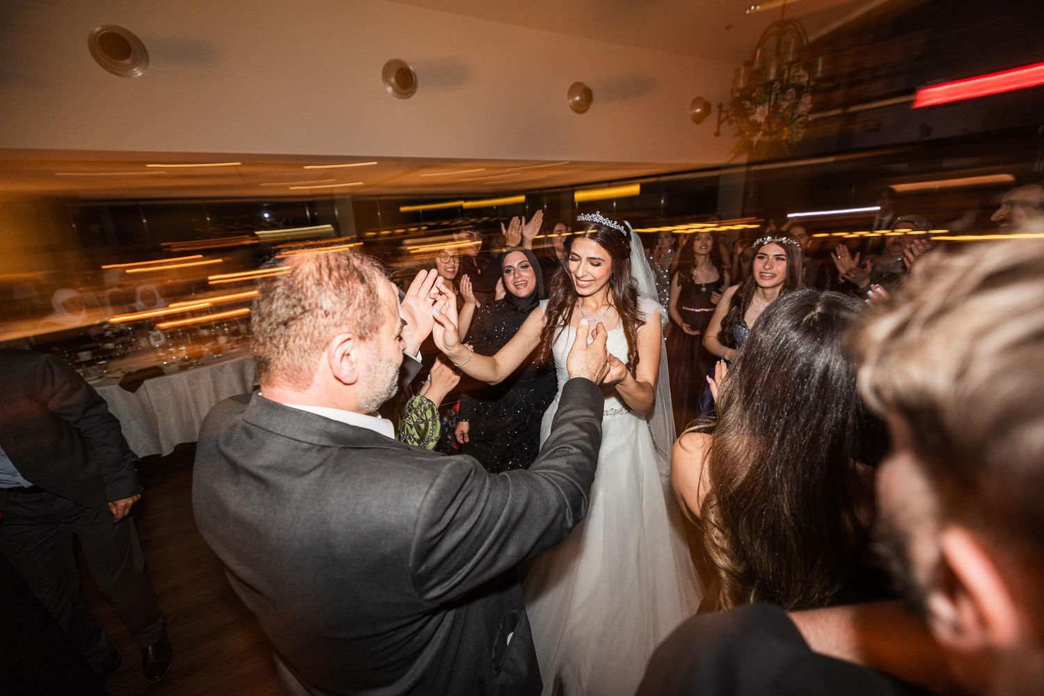 Newlyweds and guests dancing joyfully at a dimly lit wedding reception.