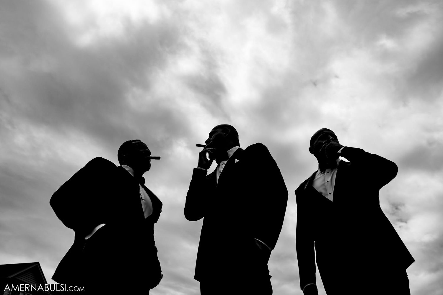 Silhouette of three people in suits against dramatic cloudy sky.