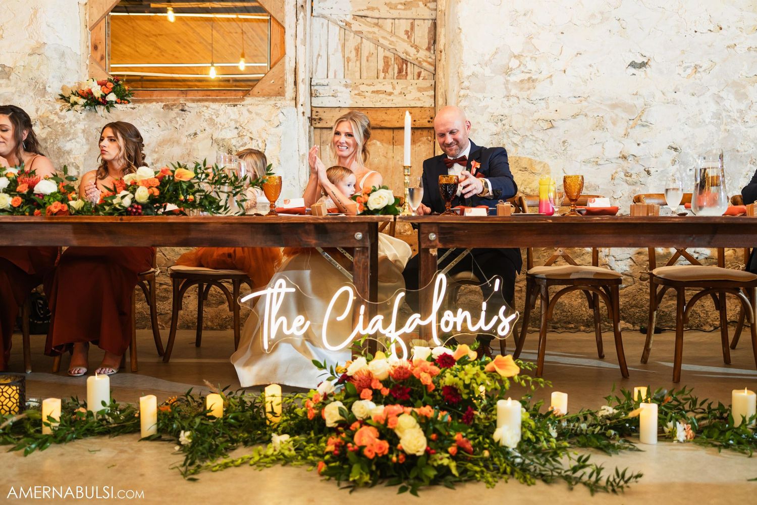 Wedding reception table decorated with lush floral arrangements and neon sign in rustic venue.