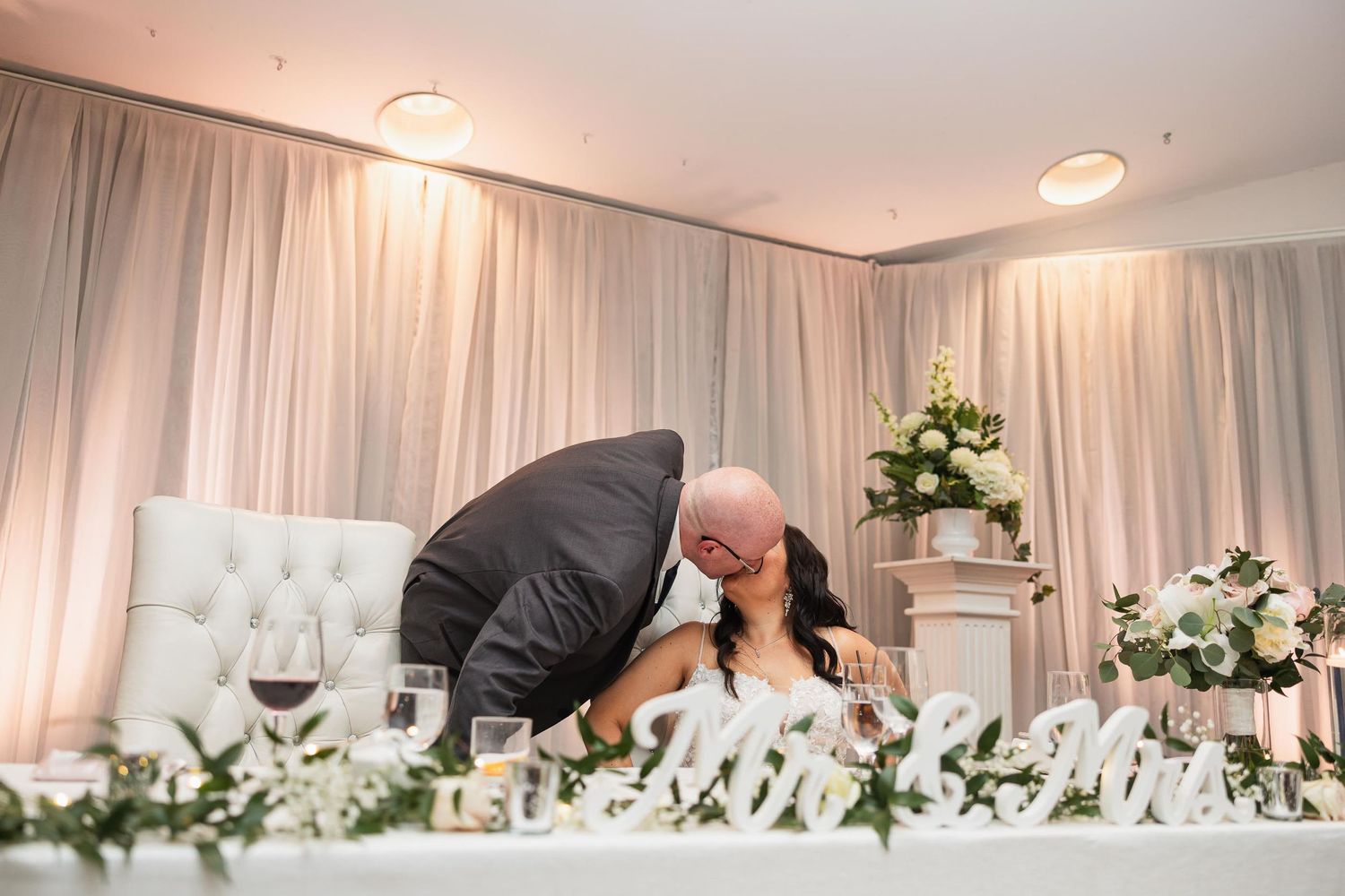 A romantic moment captured at the head table during a wedding reception.