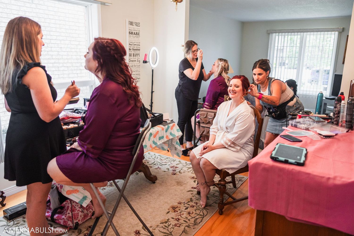Group getting ready in room with pink table cloth and makeup supplies.