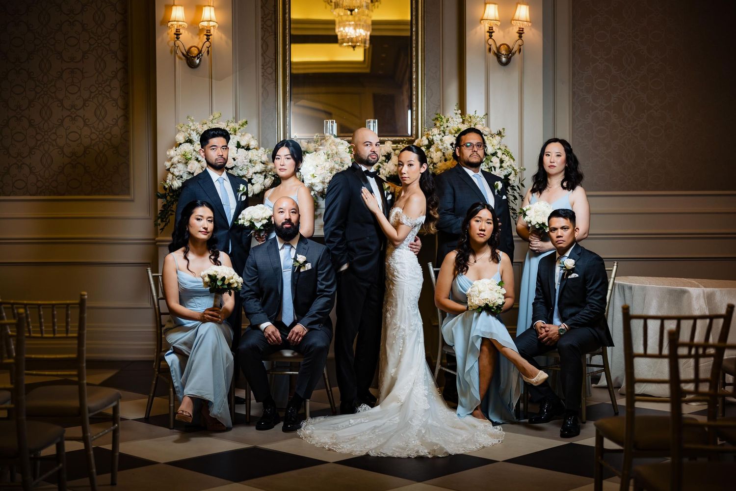 Wedding party poses formally in elegant room with chandelier and brown wall panels.