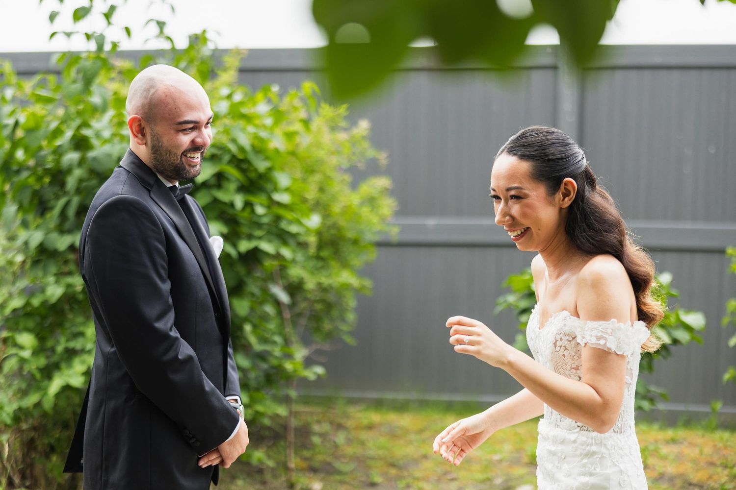 Candid moment of couple in wedding attire sharing a laugh in garden setting.