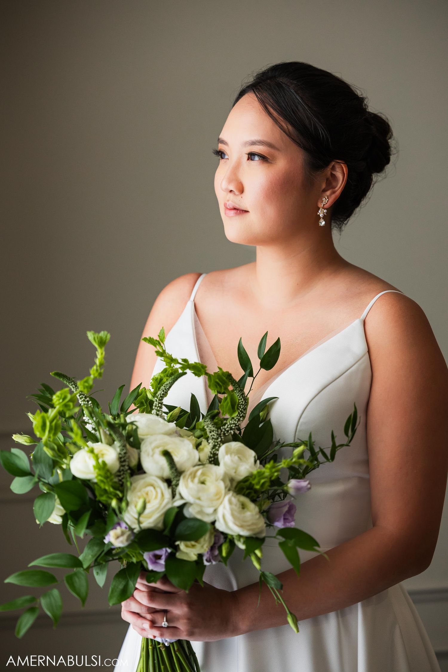 Bride in elegant white dress holds stunning white and green bouquet in portrait session.