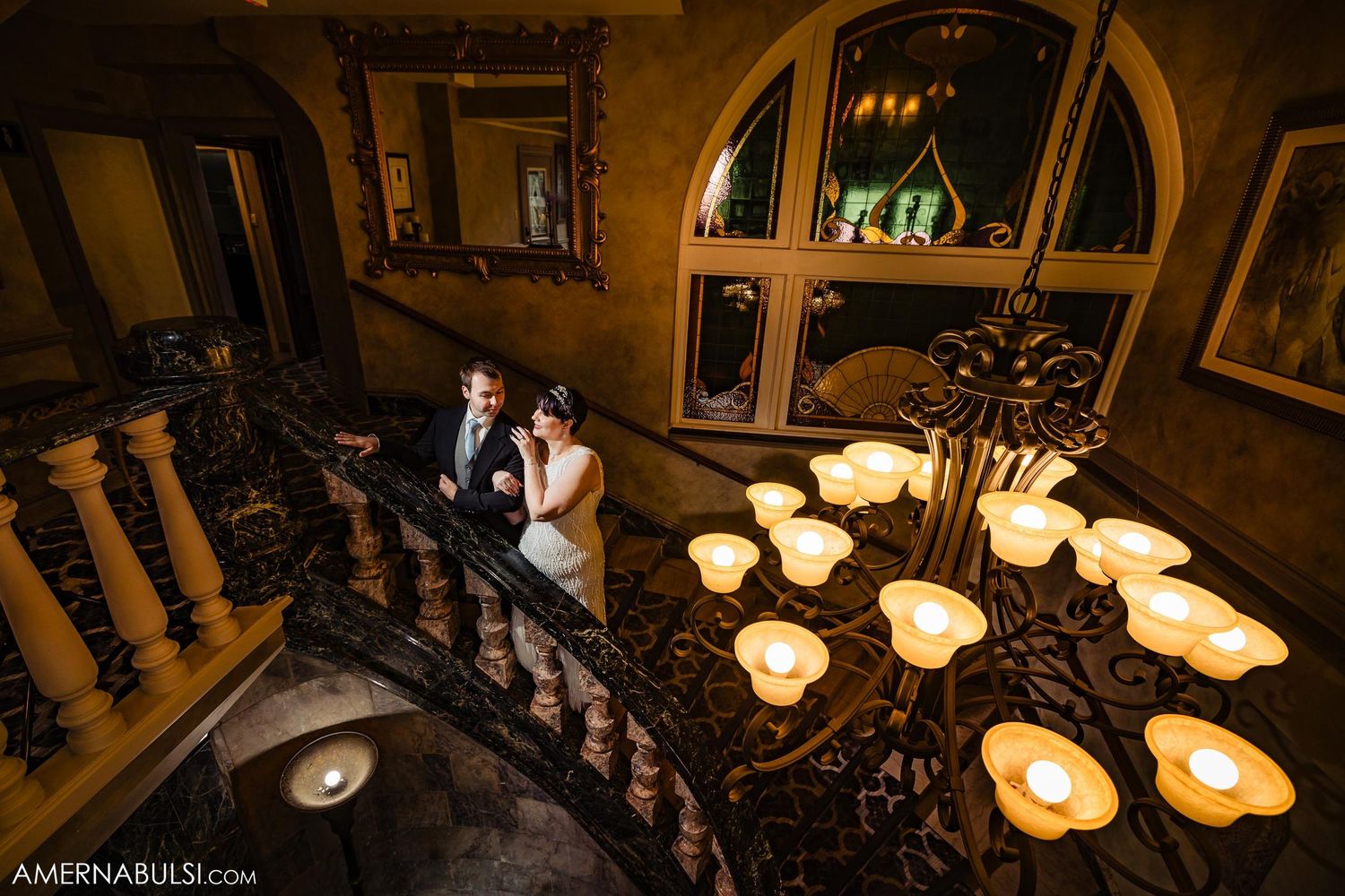 Wedding couple on elegant staircase illuminated by warm candlelight.