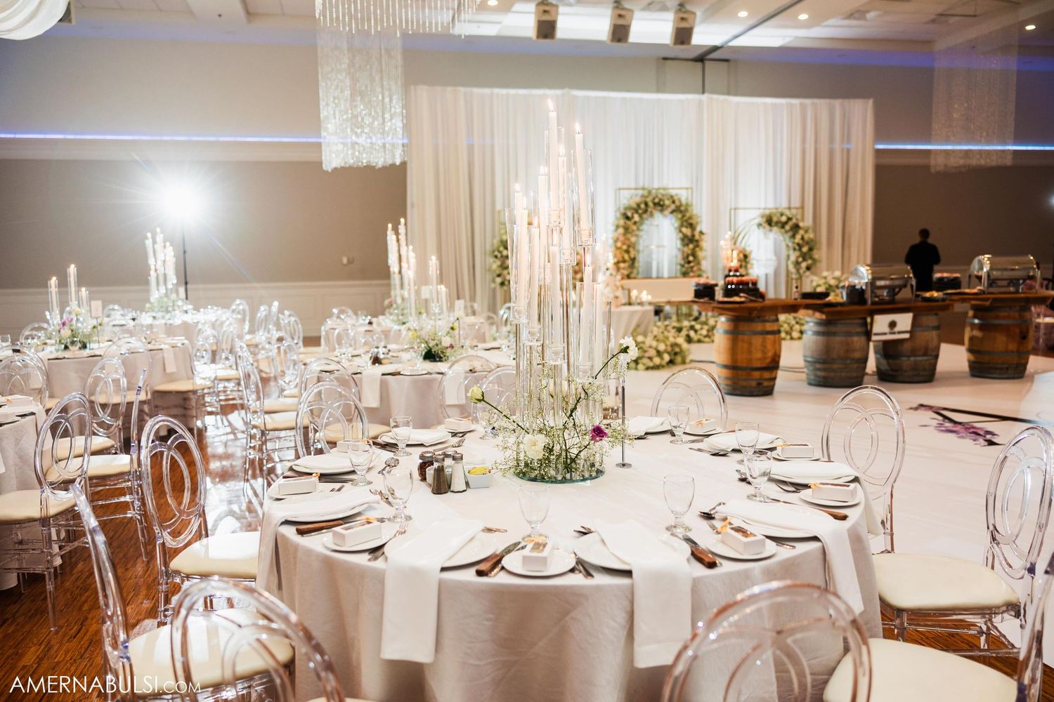 Luxurious wedding reception venue with round tables, crystal chandeliers, and floral arch decorations.