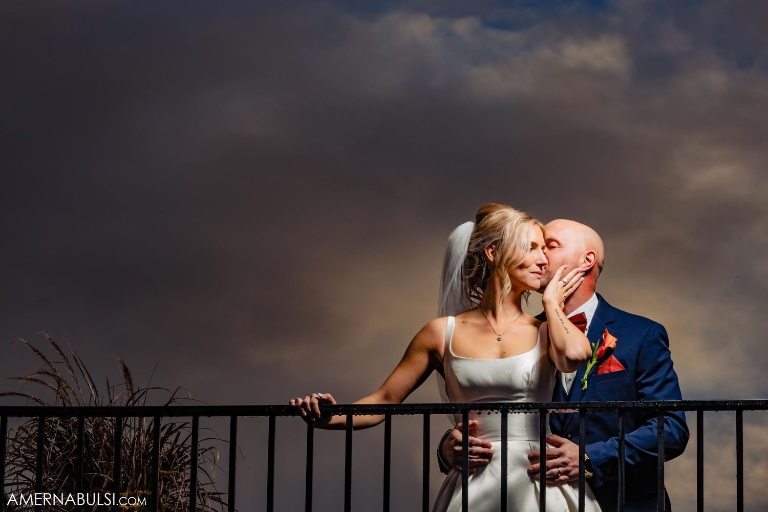 Dramatic wedding portrait of couple against dark stormy sky on balcony.