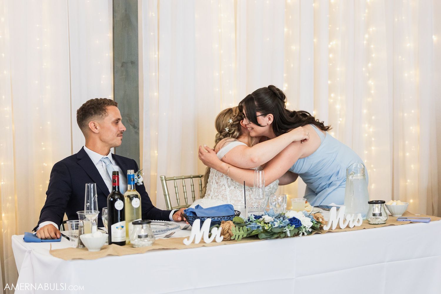 Wedding reception party with formal table settings and guests socializing in a white-lit banquet hall.