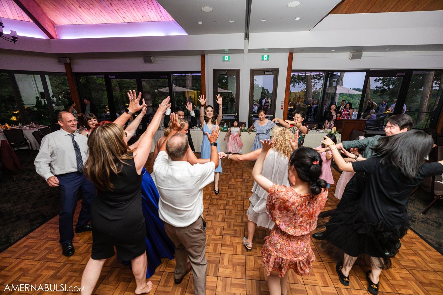 Wedding guests dancing and celebrating with raised arms on a wooden dance floor.