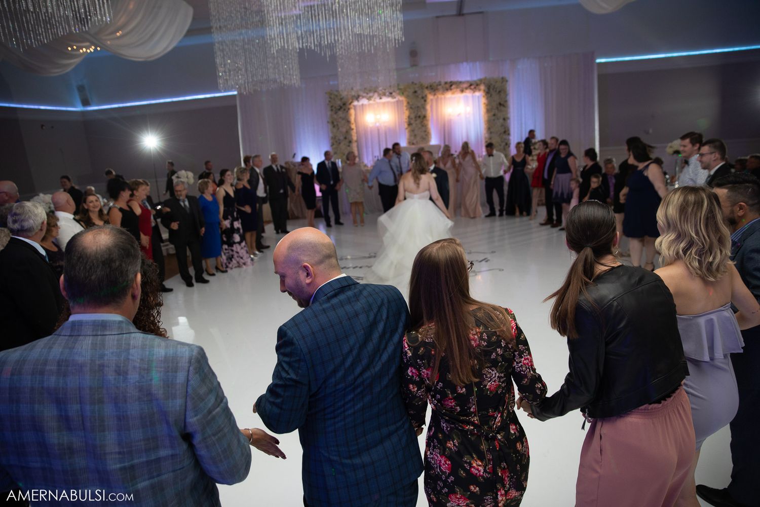 Wedding guests gathered on dance floor during evening reception celebration.