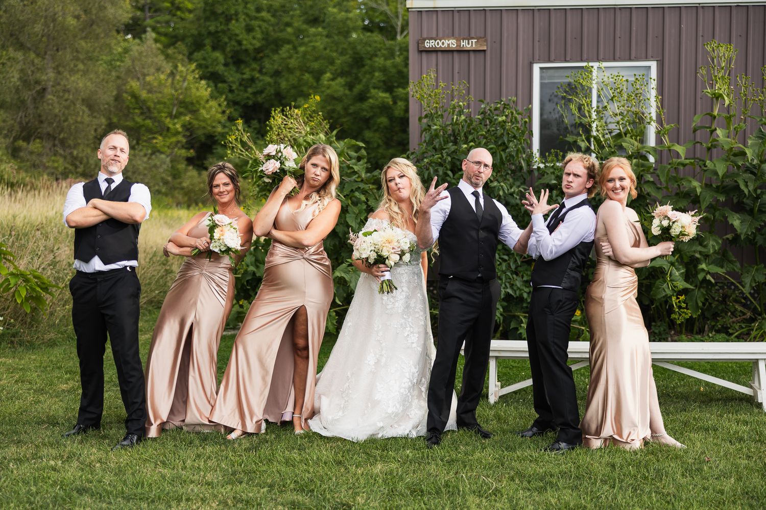Wedding party in pink bridesmaid dresses and dark suits poses together on a green garden path in summer.
