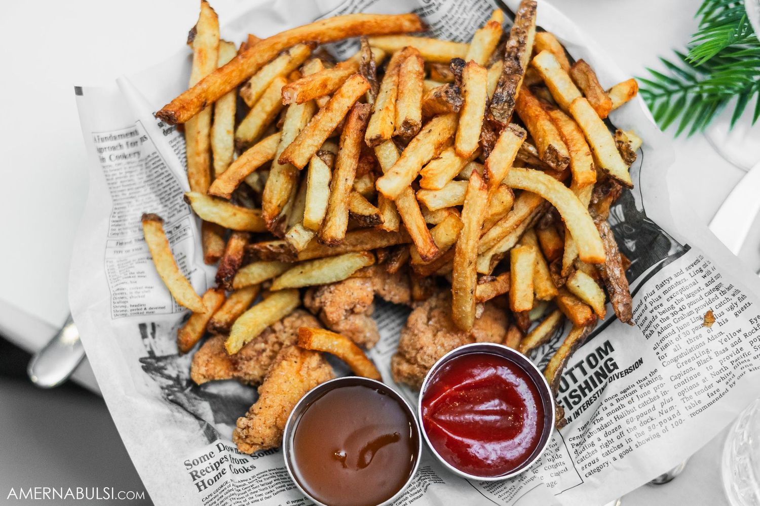 Golden crispy french fries served on newspaper with ketchup and chocolate dipping sauces.
