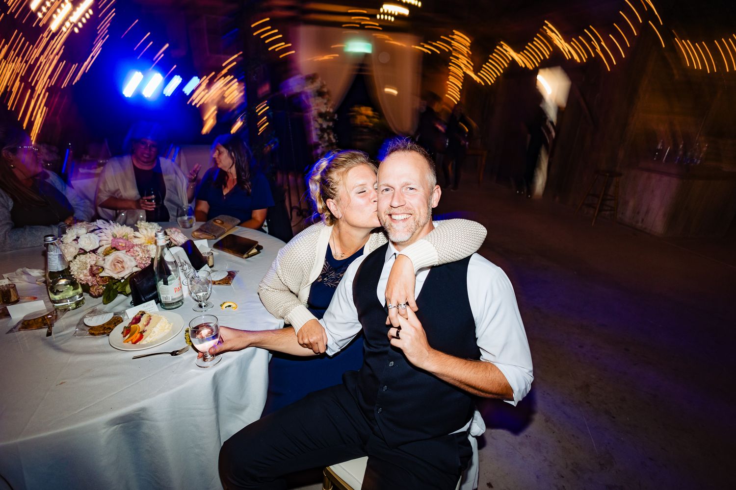 Wedding guests dancing and celebrating on the dance floor at a dimly lit reception venue.