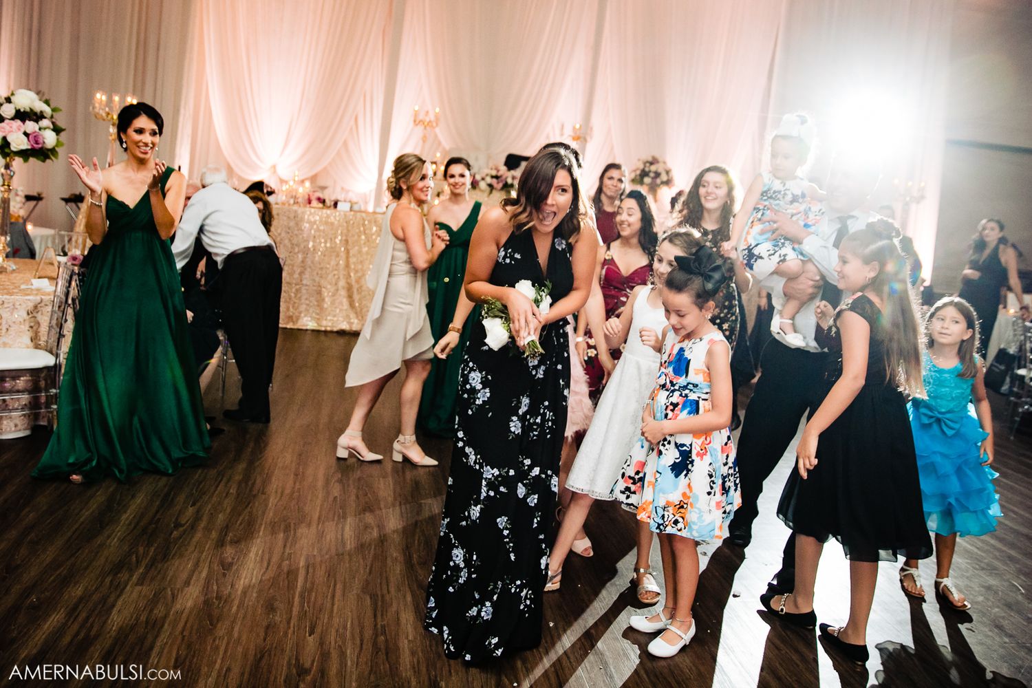 Wedding guests dance and celebrate together on a wooden dance floor during a reception party.