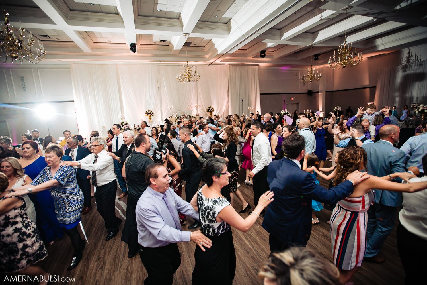 Couples dancing together at an elegant wedding reception in a grand ballroom with white decor.