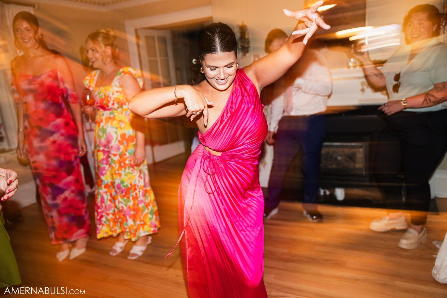 Dancer in vibrant pink dress moving energetically at indoor celebration.