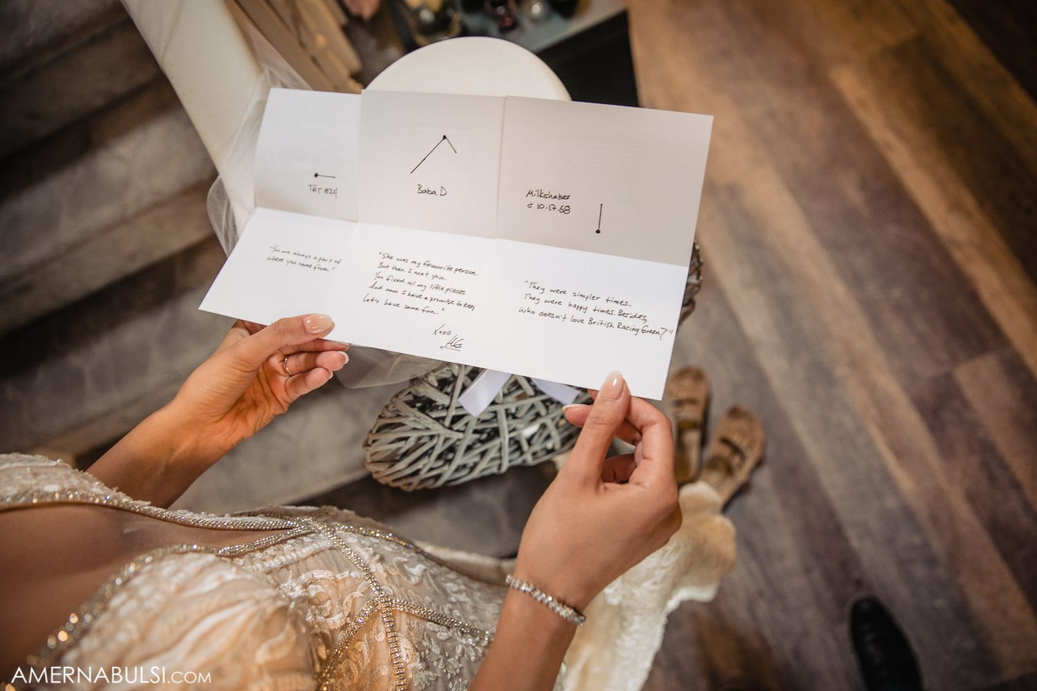 Hands holding open a wedding invitation with geometric designs on a wooden surface.