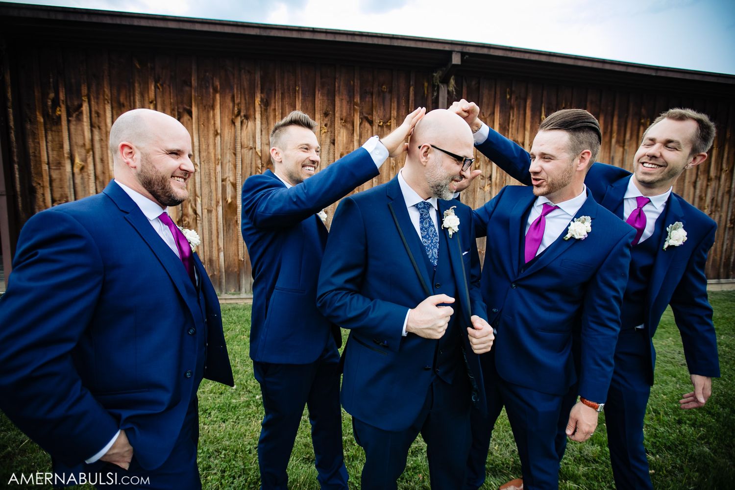 Groomsmen in navy suits share laughs during outdoor wedding photo session.