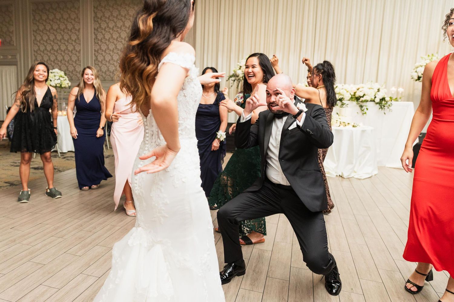 Energetic dance moves displayed during a wedding reception on a wooden dance floor.