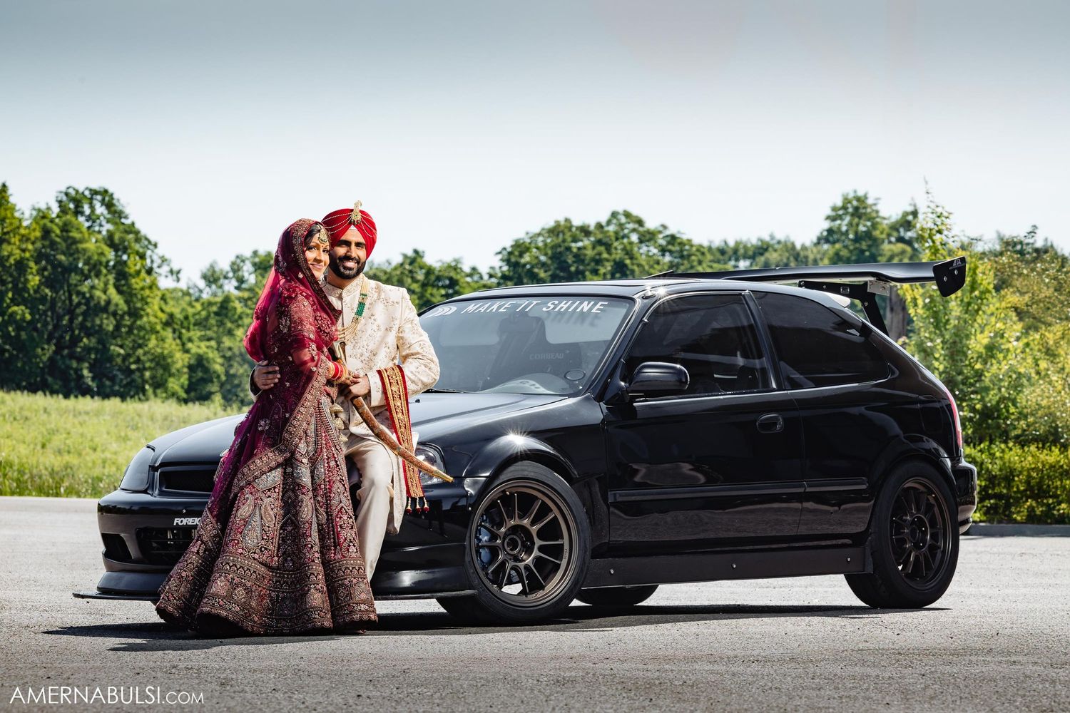 Indian wedding couple posing with black modified sports car outdoors.