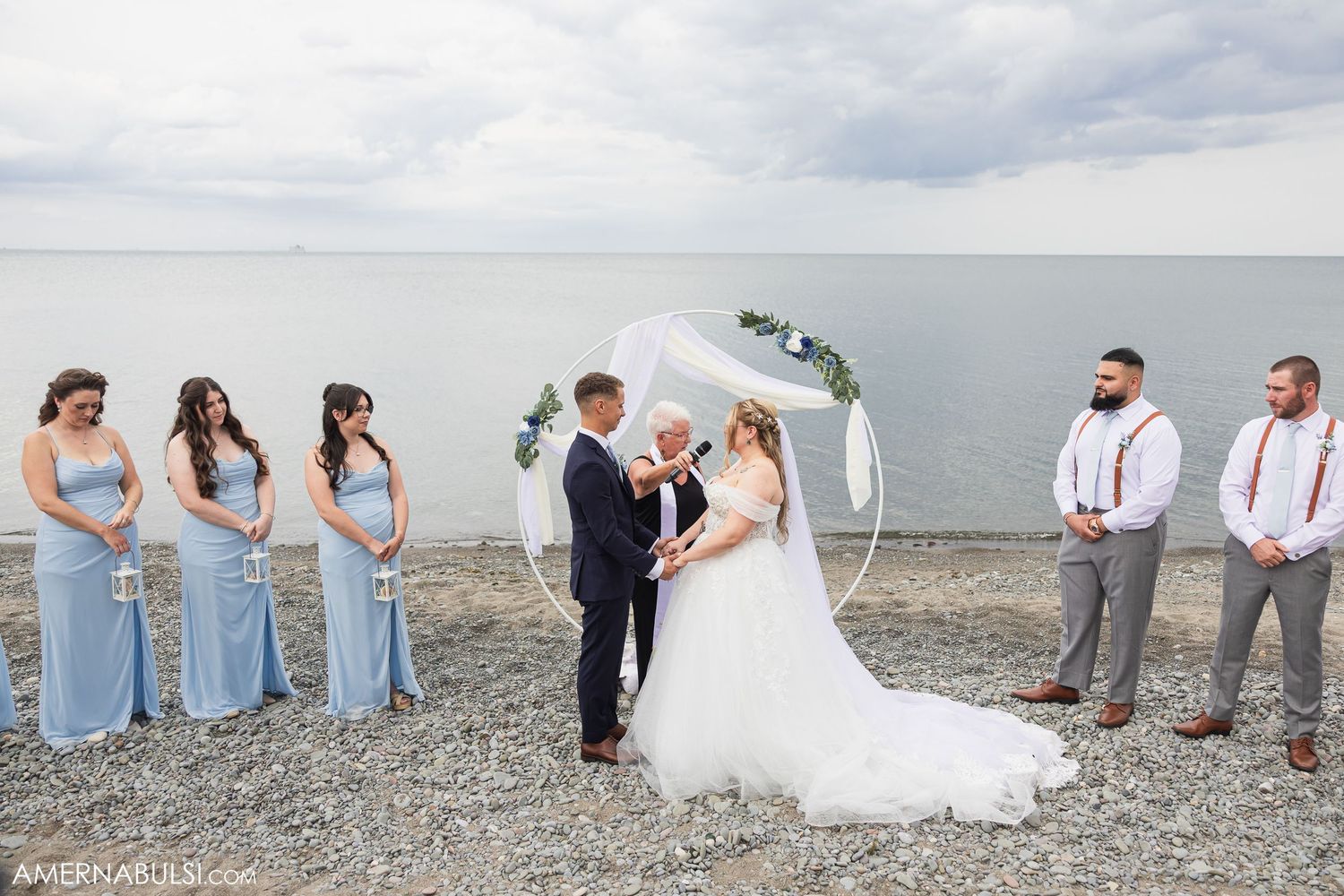 Wedding party poses for photos on rocky beach in light blue and grey attire.