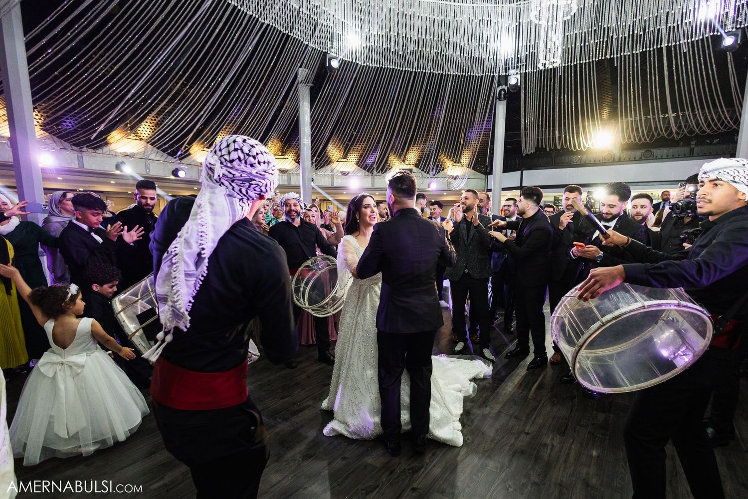 Wedding guests dancing and celebrating on a dance floor under dramatic string lighting at an elegant reception venue.