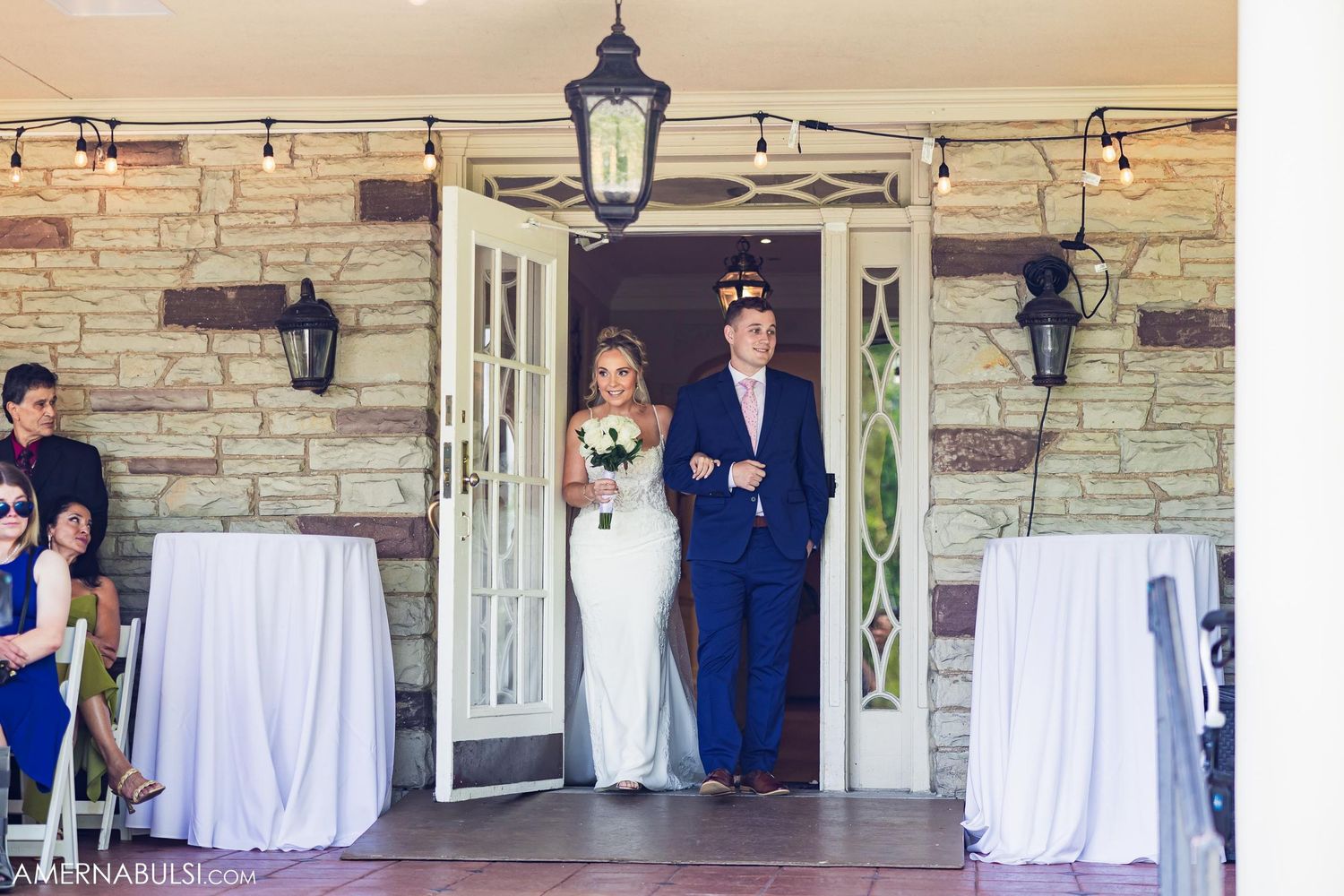 A bridal party entrance at a stone venue with decorative lanterns and white linens.