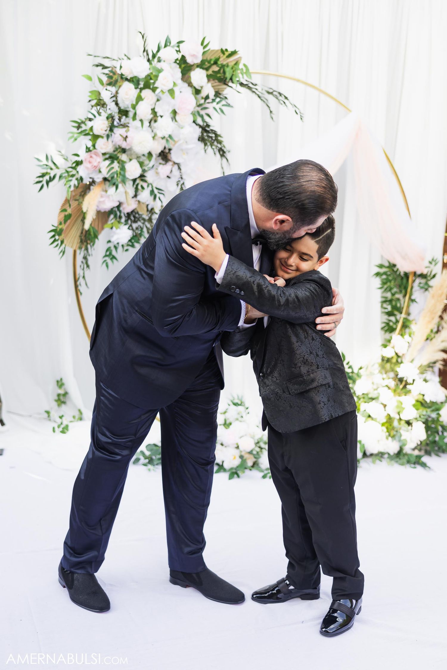 Emotional embrace captured against a white floral wedding backdrop.
