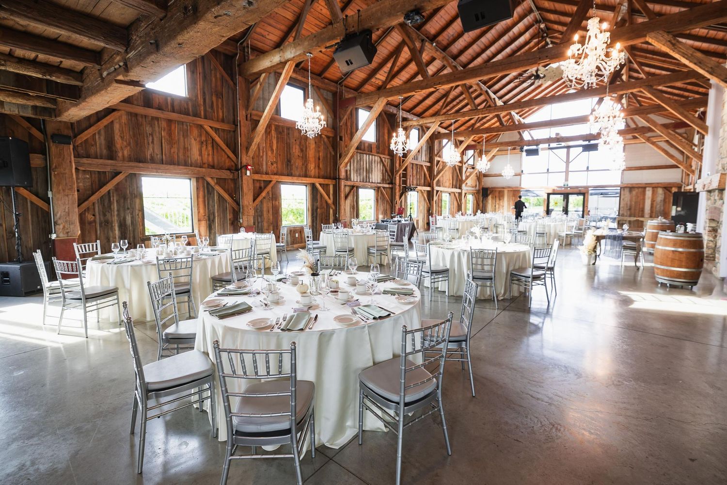 Spacious rustic barn wedding venue with exposed beams, chandeliers and round reception tables.