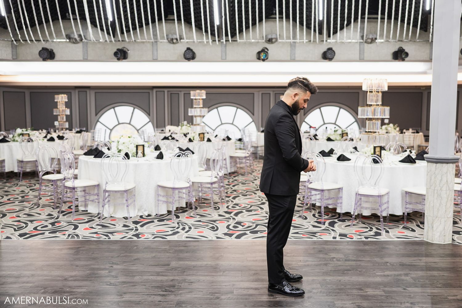 Empty wedding reception venue with white chairs and tables set up in elegant rows.