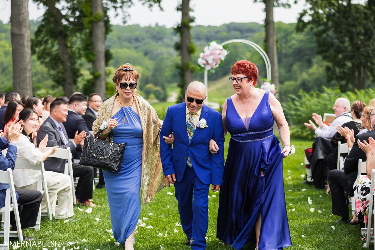 Wedding party members walking down garden path in blue formal attire.