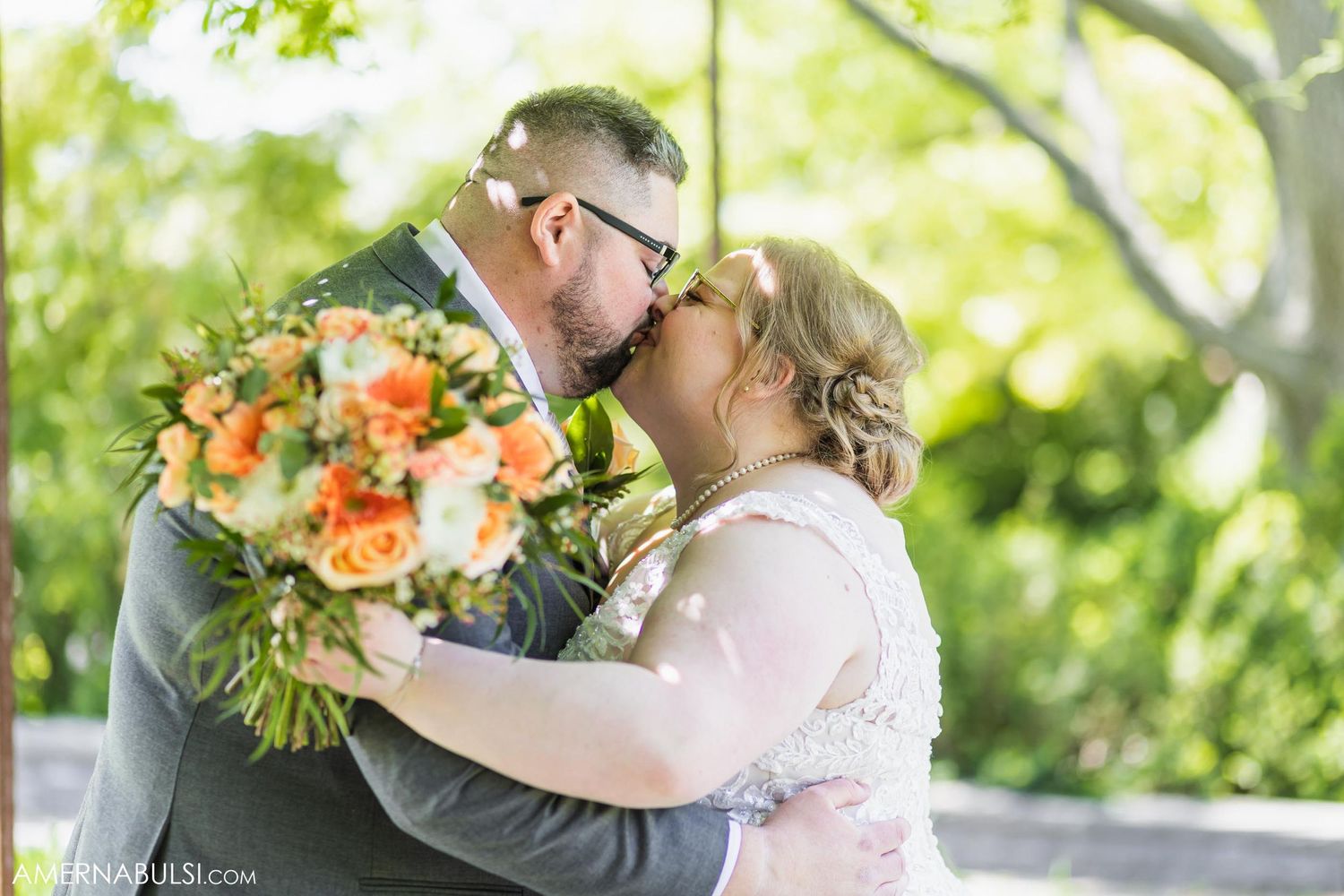 Wedding couple embraces with coral bouquet during outdoor garden ceremony.