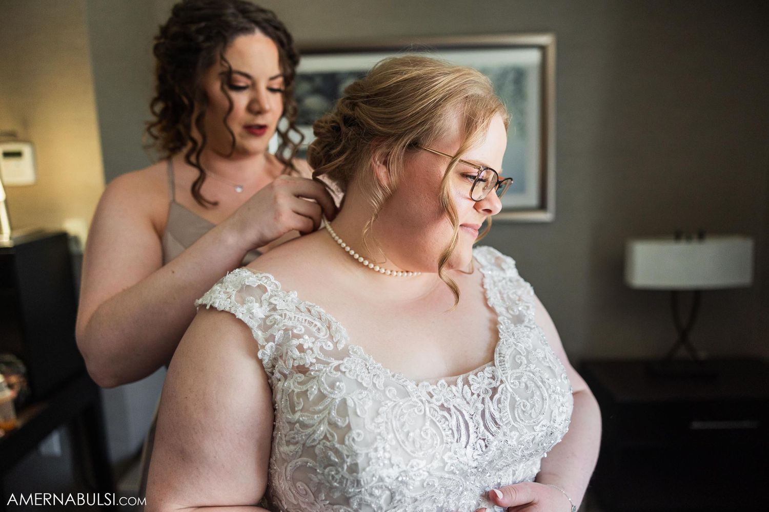 Bride in lace wedding dress getting help with final preparations before her special day.
