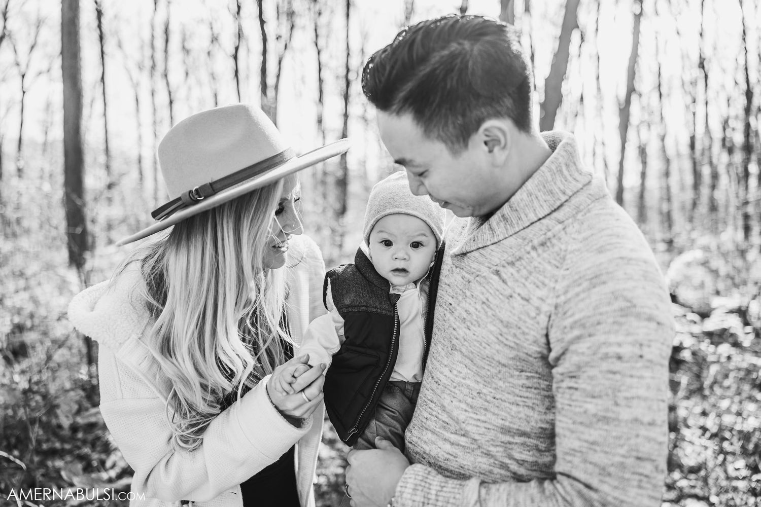 Family with baby bundled in warm clothing pose together in winter woods setting.