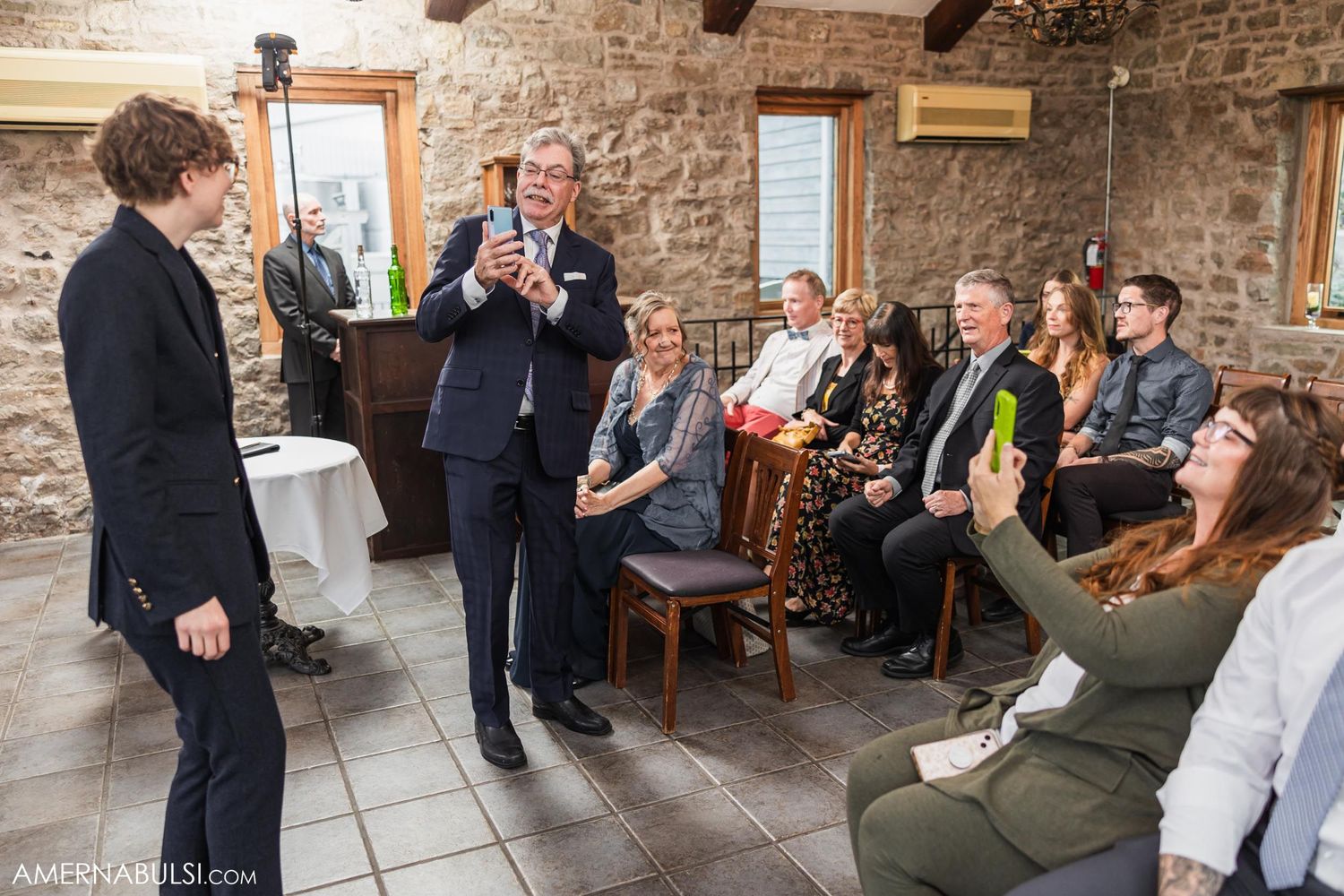 Guests gathered in stone-walled room during wedding celebration.