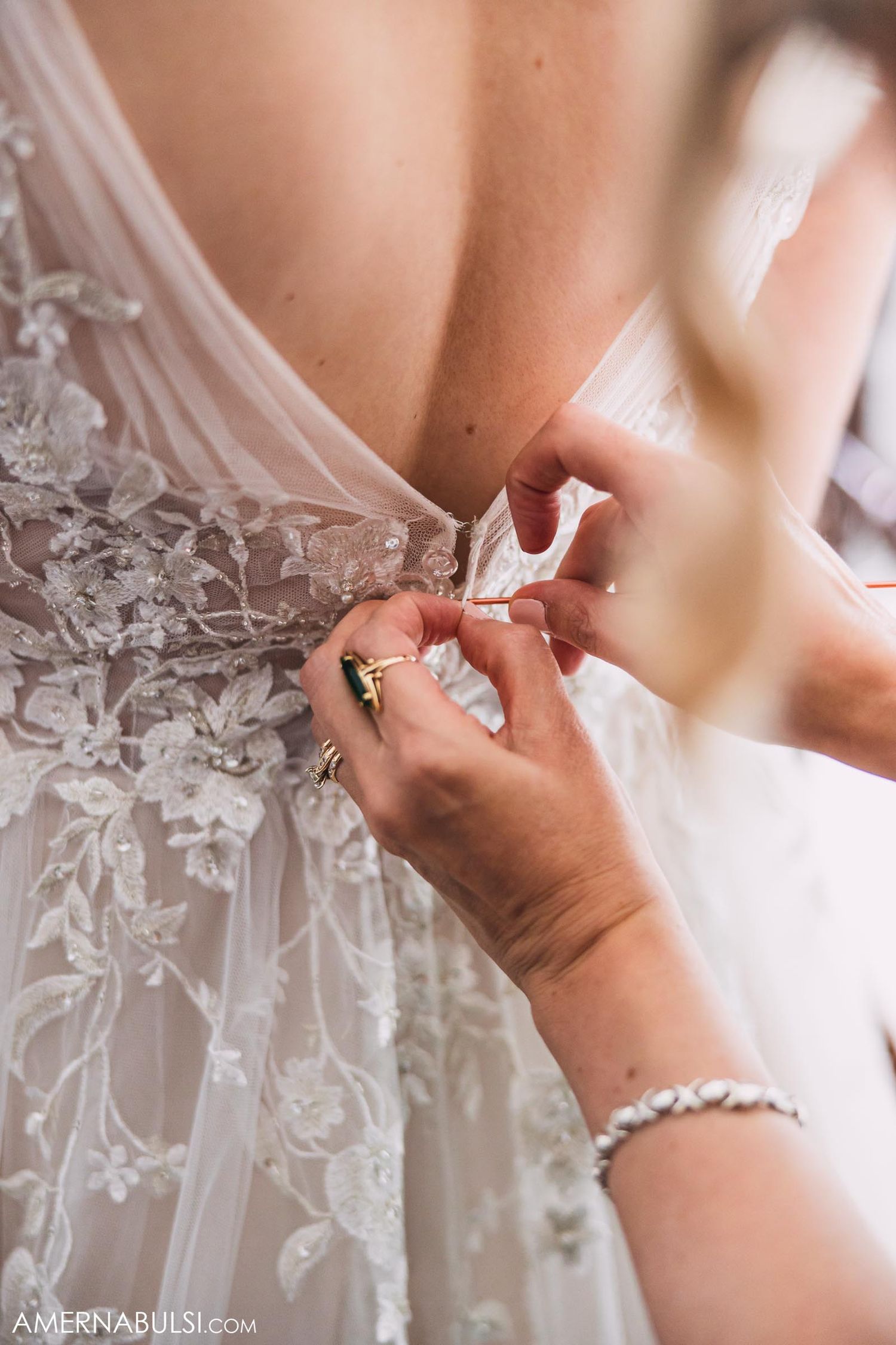 Close-up detail of hands fastening delicate buttons on back of lace wedding dress.