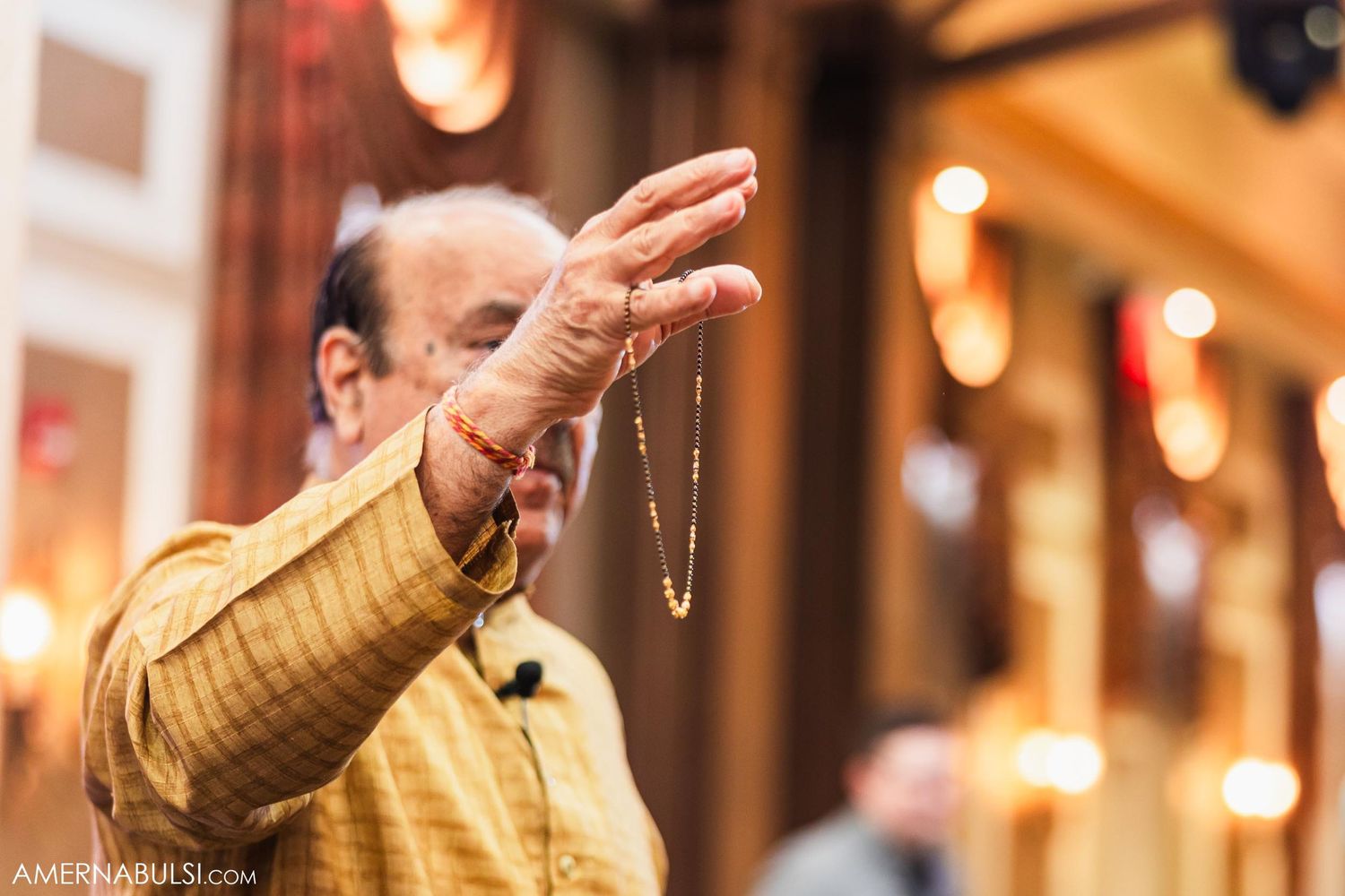Elder performing blessing ritual with ceremonial beads during traditional Indian wedding ceremony.