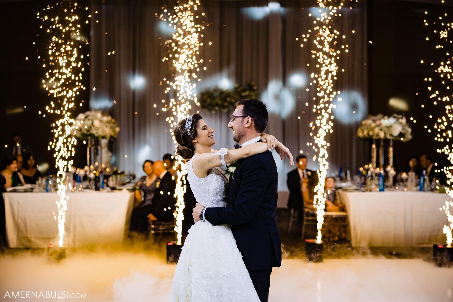 Wedding couple dancing surrounded by sparkling pyrotechnic effects in an elegant reception hall.